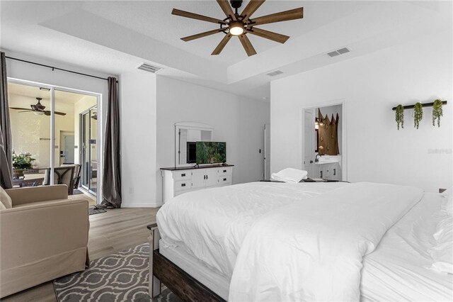 bedroom with ensuite bath, visible vents, a raised ceiling, and wood finished floors