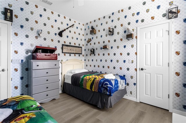 bedroom with baseboards, light wood-type flooring, visible vents, and wallpapered walls