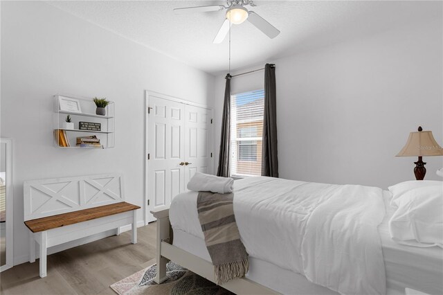 bedroom with light wood-style floors, ceiling fan, baseboards, and a closet