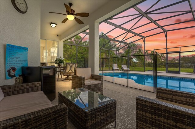 pool at dusk featuring outdoor lounge area, ceiling fan, a patio area, and glass enclosure