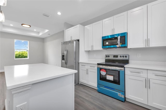 kitchen featuring a tray ceiling, hardwood / wood-style flooring, white cabinets, and appliances with stainless steel finishes