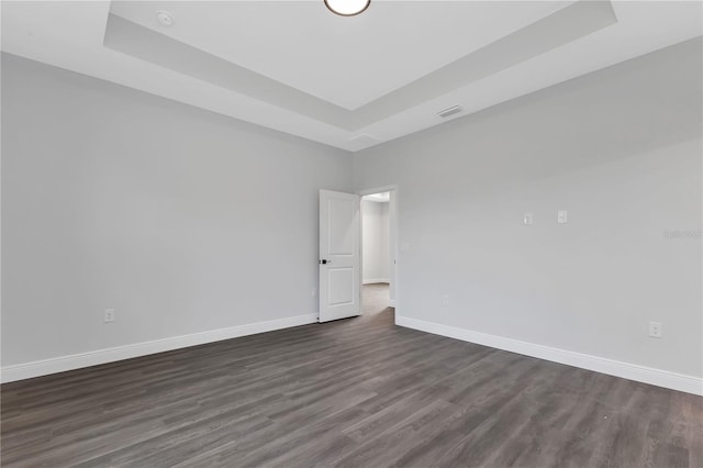 empty room with dark hardwood / wood-style flooring and a raised ceiling