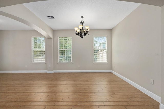 spare room with a chandelier, light hardwood / wood-style flooring, and a textured ceiling