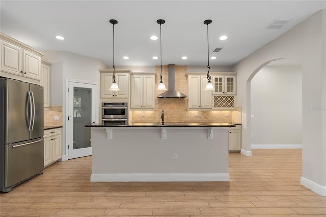 kitchen featuring wall chimney range hood, stainless steel fridge, a center island with sink, a breakfast bar area, and backsplash