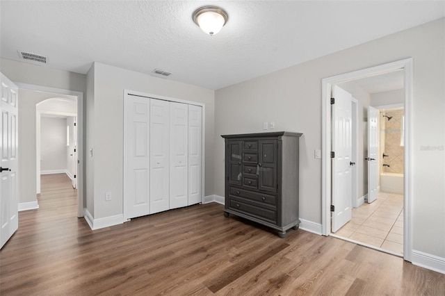 unfurnished bedroom featuring a textured ceiling, a closet, ensuite bathroom, and hardwood / wood-style floors