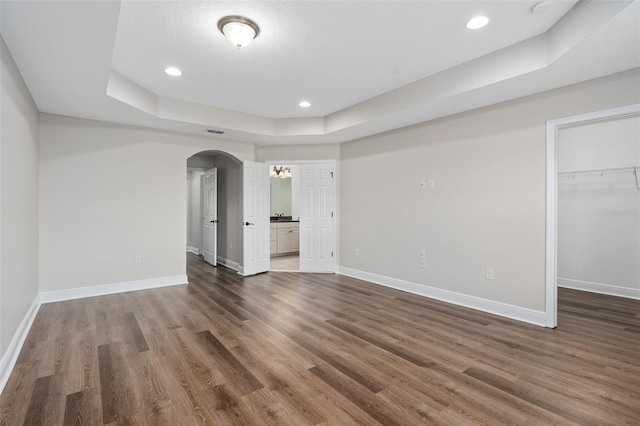 unfurnished bedroom featuring a walk in closet, a raised ceiling, and dark hardwood / wood-style floors