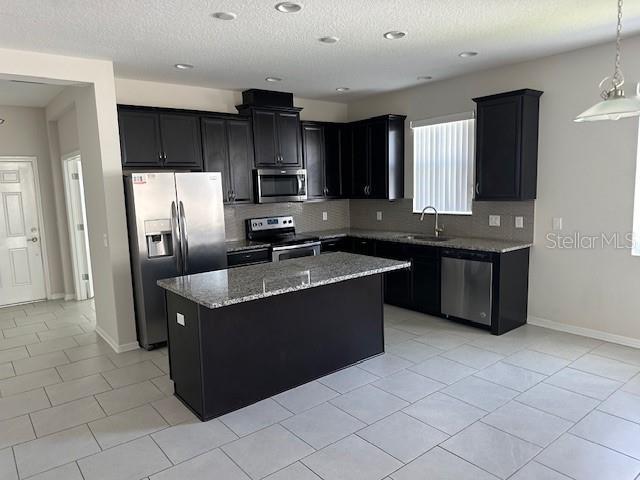 kitchen featuring sink, stainless steel appliances, light tile patterned floors, light stone counters, and a kitchen island