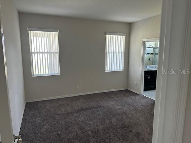 spare room featuring dark colored carpet and a healthy amount of sunlight