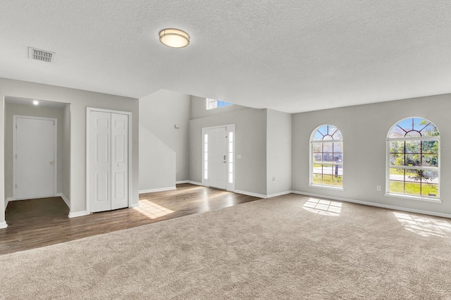 unfurnished living room featuring a wealth of natural light, dark carpet, and a textured ceiling