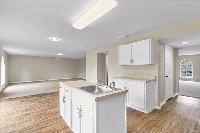 kitchen with white cabinets, sink, an island with sink, and light wood-type flooring