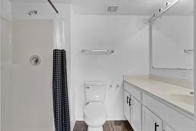 bathroom with hardwood / wood-style floors, vanity, toilet, a textured ceiling, and walk in shower