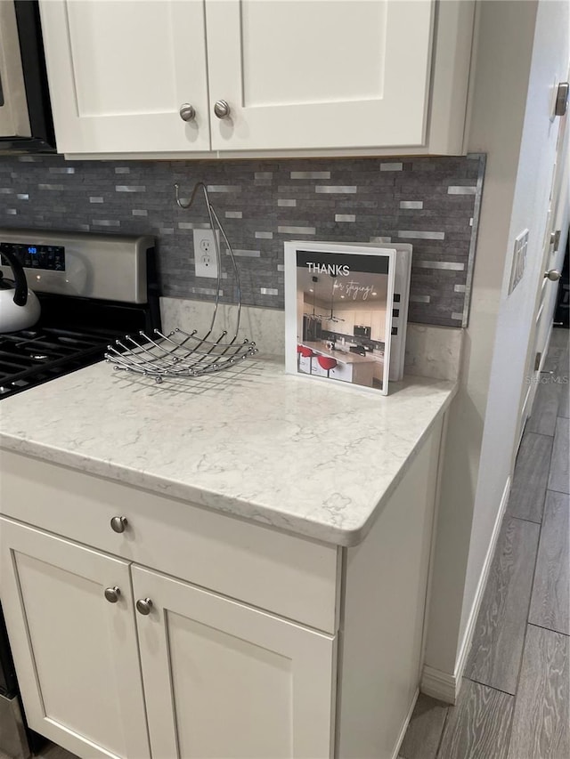 kitchen with white gas stove, light stone counters, wood-type flooring, and backsplash