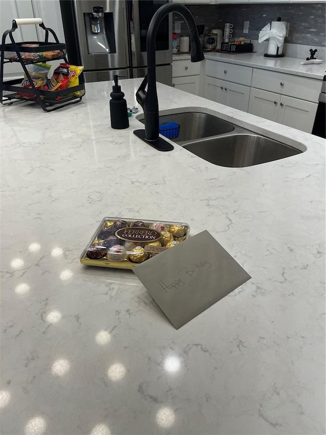 kitchen featuring sink, stainless steel fridge, tasteful backsplash, light stone counters, and white cabinetry