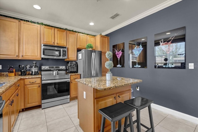 kitchen featuring light stone countertops, appliances with stainless steel finishes, crown molding, light tile patterned floors, and a center island