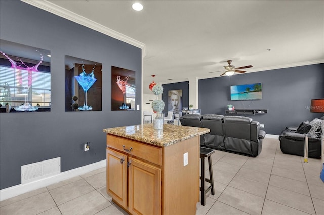 kitchen with light tile patterned floors, a center island, ceiling fan, and ornamental molding