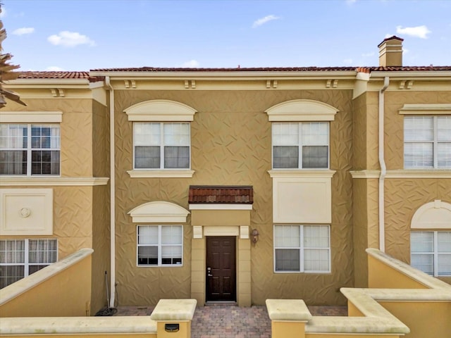 townhome / multi-family property with a chimney, a tile roof, and stucco siding