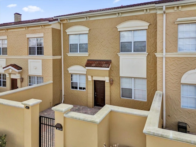 multi unit property featuring a chimney, a gate, fence, and stucco siding