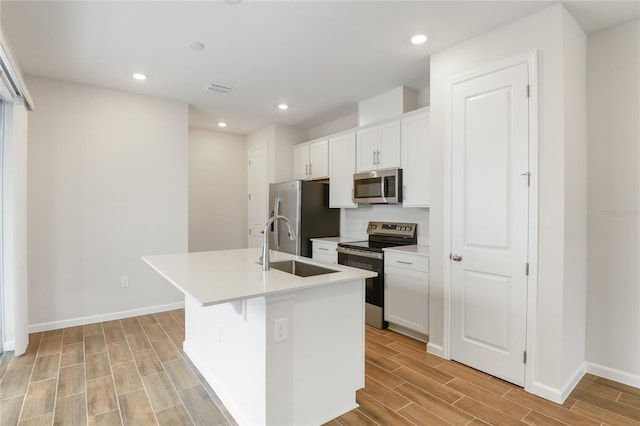 kitchen featuring white cabinetry, sink, stainless steel appliances, an island with sink, and light wood-type flooring