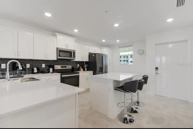 kitchen featuring sink, appliances with stainless steel finishes, a kitchen bar, white cabinets, and a kitchen island