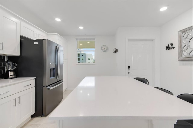 kitchen featuring white cabinetry, stainless steel fridge with ice dispenser, a breakfast bar area, and a kitchen island