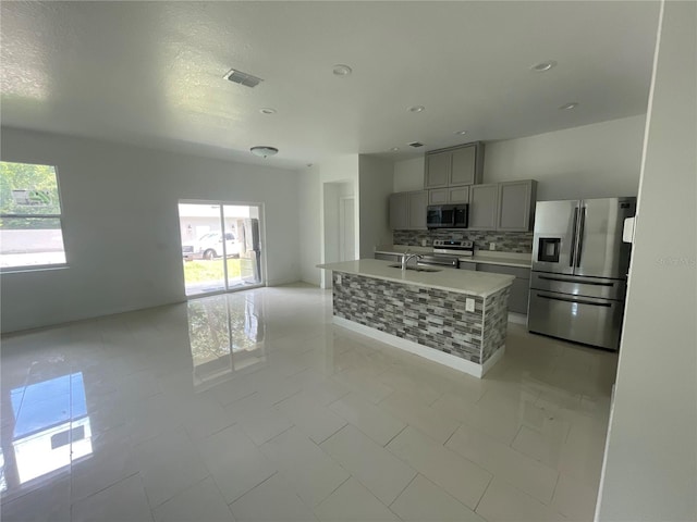 kitchen with backsplash, gray cabinetry, stainless steel appliances, sink, and a center island with sink