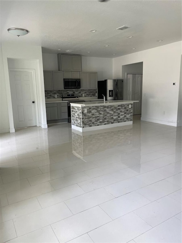 kitchen with a large island, sink, stainless steel appliances, gray cabinets, and decorative backsplash