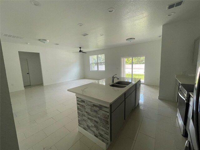 kitchen with sink, stainless steel electric range oven, ceiling fan, and an island with sink