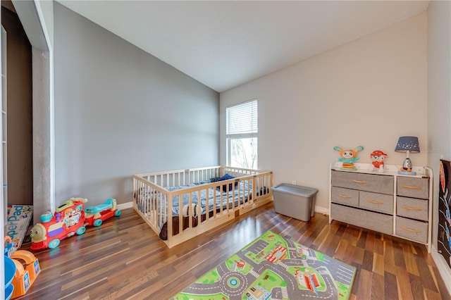 bedroom featuring vaulted ceiling, dark hardwood / wood-style flooring, and a nursery area