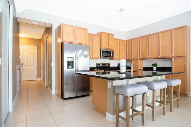 kitchen featuring light tile patterned floors, sink, a breakfast bar area, appliances with stainless steel finishes, and an island with sink