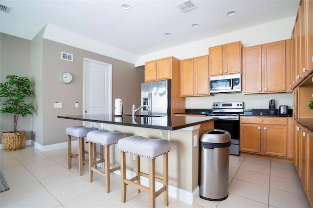 kitchen featuring light tile patterned floors, a breakfast bar area, stainless steel appliances, and an island with sink