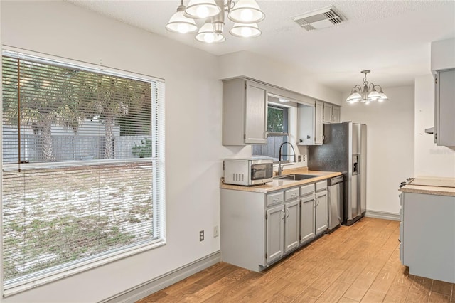 kitchen with stainless steel appliances, sink, pendant lighting, an inviting chandelier, and light hardwood / wood-style floors