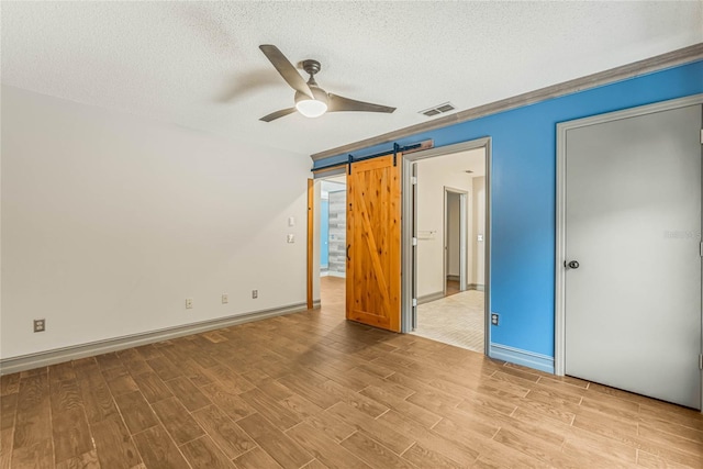 unfurnished bedroom featuring ceiling fan, a barn door, light wood-type flooring, and a textured ceiling