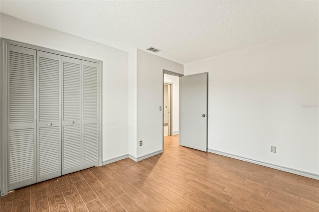 unfurnished bedroom featuring light wood-type flooring, a textured ceiling, and a closet