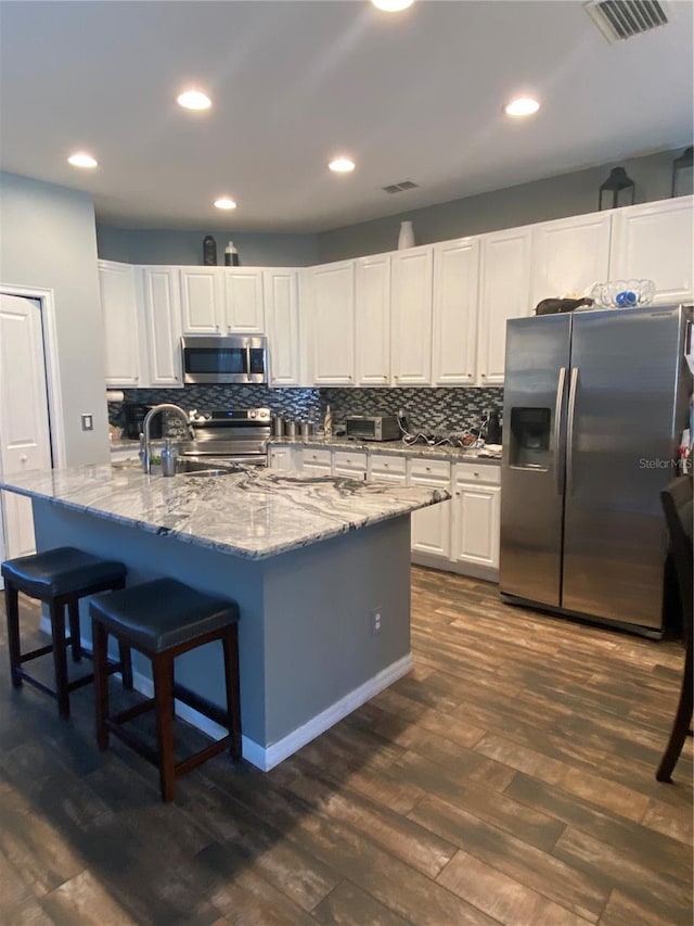 kitchen featuring a kitchen island with sink, dark hardwood / wood-style floors, light stone countertops, appliances with stainless steel finishes, and white cabinetry