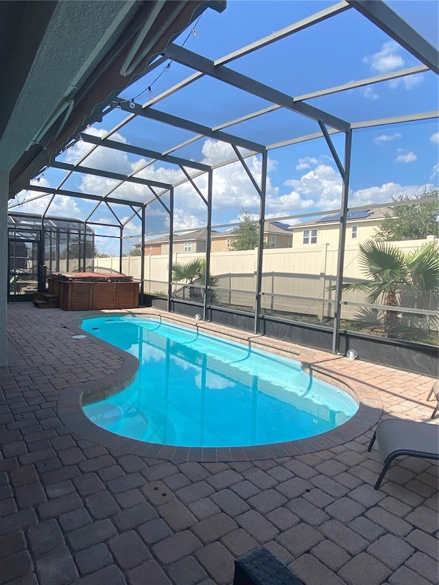 view of pool featuring a patio, glass enclosure, and a hot tub