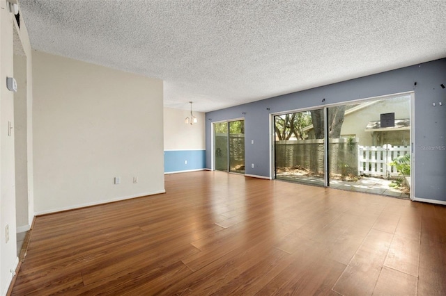 empty room with a chandelier, hardwood / wood-style floors, and a textured ceiling