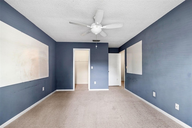 unfurnished bedroom with light carpet, a walk in closet, a textured ceiling, ceiling fan, and a closet