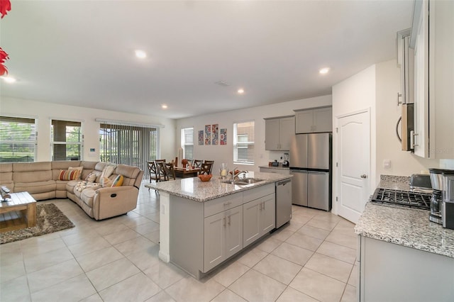 kitchen featuring appliances with stainless steel finishes, light stone counters, a kitchen island with sink, sink, and gray cabinets