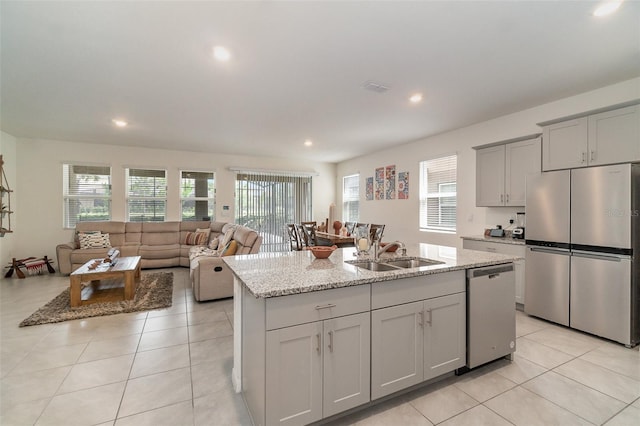 kitchen featuring light stone countertops, appliances with stainless steel finishes, sink, light tile patterned floors, and a center island with sink