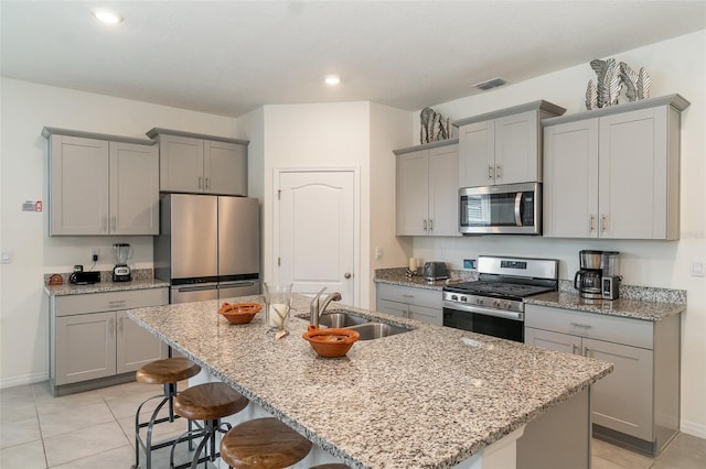 kitchen featuring a kitchen island with sink, sink, stainless steel appliances, and light stone counters