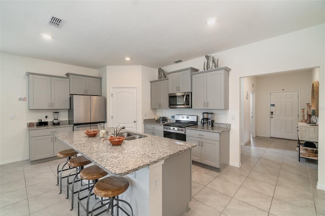 kitchen featuring a breakfast bar, stainless steel appliances, a kitchen island with sink, sink, and gray cabinets