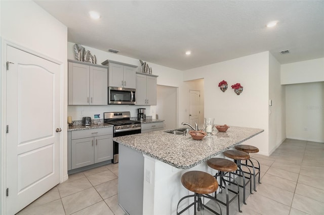 kitchen featuring gray cabinets, sink, an island with sink, and stainless steel appliances