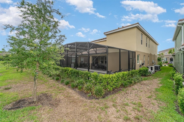 back of house with glass enclosure and a yard