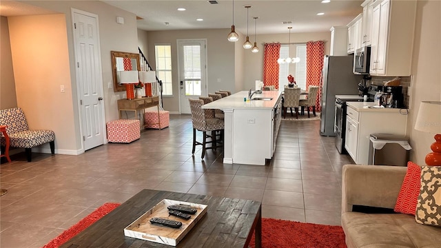 kitchen with pendant lighting, a breakfast bar area, appliances with stainless steel finishes, white cabinets, and a center island with sink