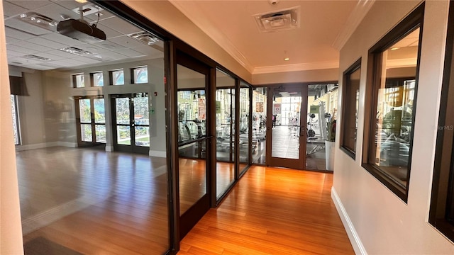 corridor with crown molding, french doors, and light wood-type flooring