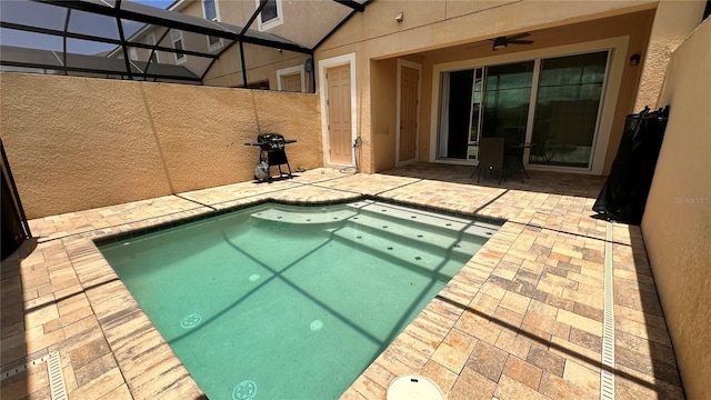 view of swimming pool with ceiling fan, a patio, and glass enclosure