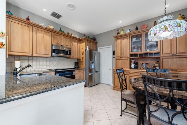 kitchen featuring backsplash, dark stone counters, sink, decorative light fixtures, and stainless steel appliances