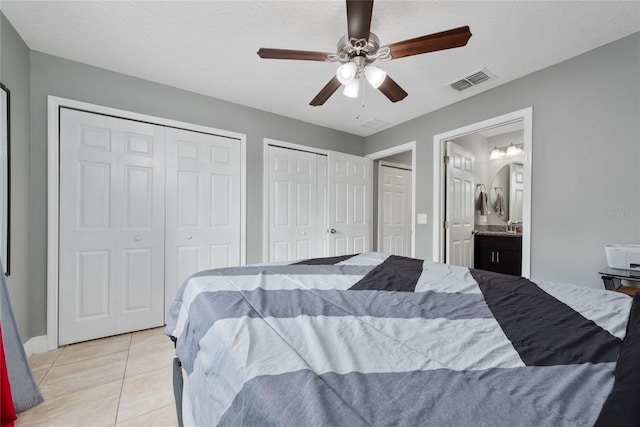 bedroom with a textured ceiling, two closets, light tile patterned flooring, ceiling fan, and ensuite bathroom