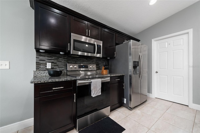 kitchen with appliances with stainless steel finishes, decorative backsplash, light tile patterned flooring, dark stone countertops, and dark brown cabinets