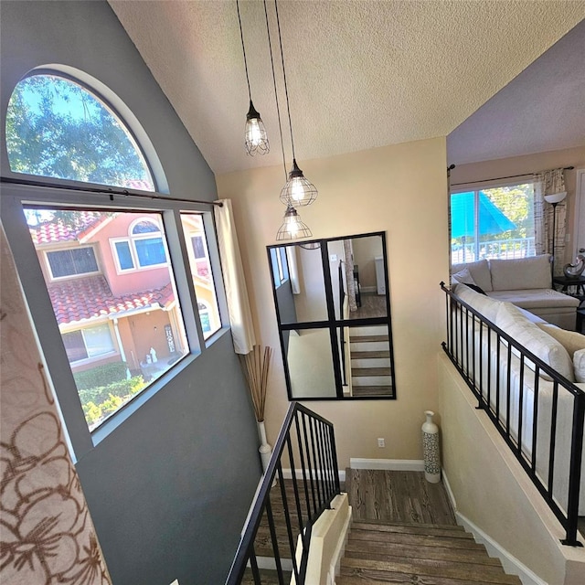 stairway featuring plenty of natural light, wood-type flooring, a textured ceiling, and vaulted ceiling